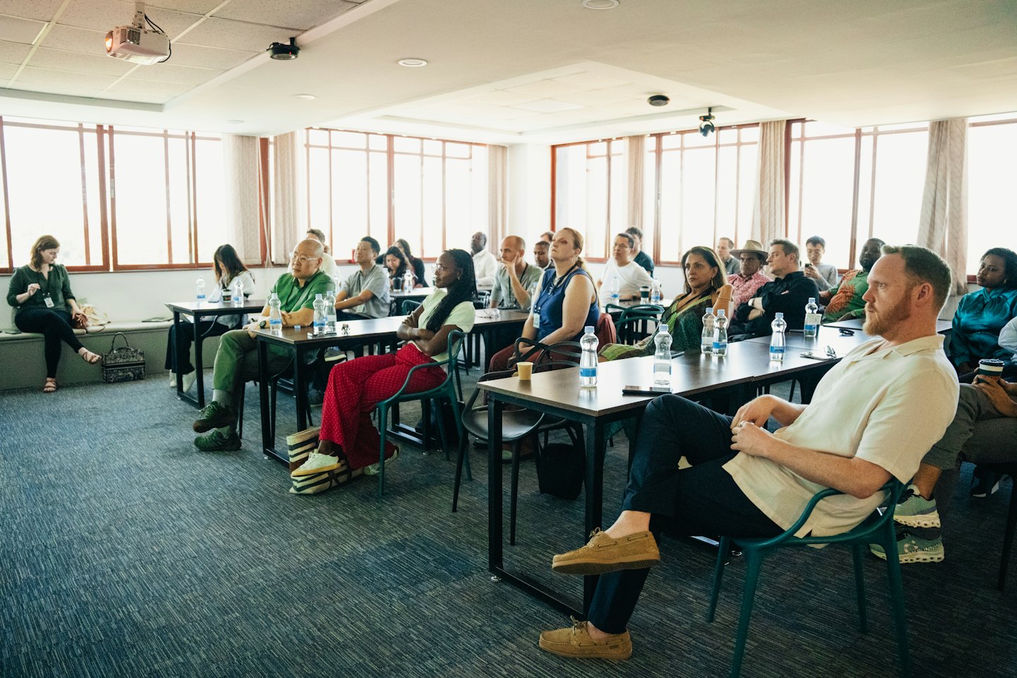 Dorośli uczestniczą w profesjonalnej konferencji, robiąc notatki przy stołach.