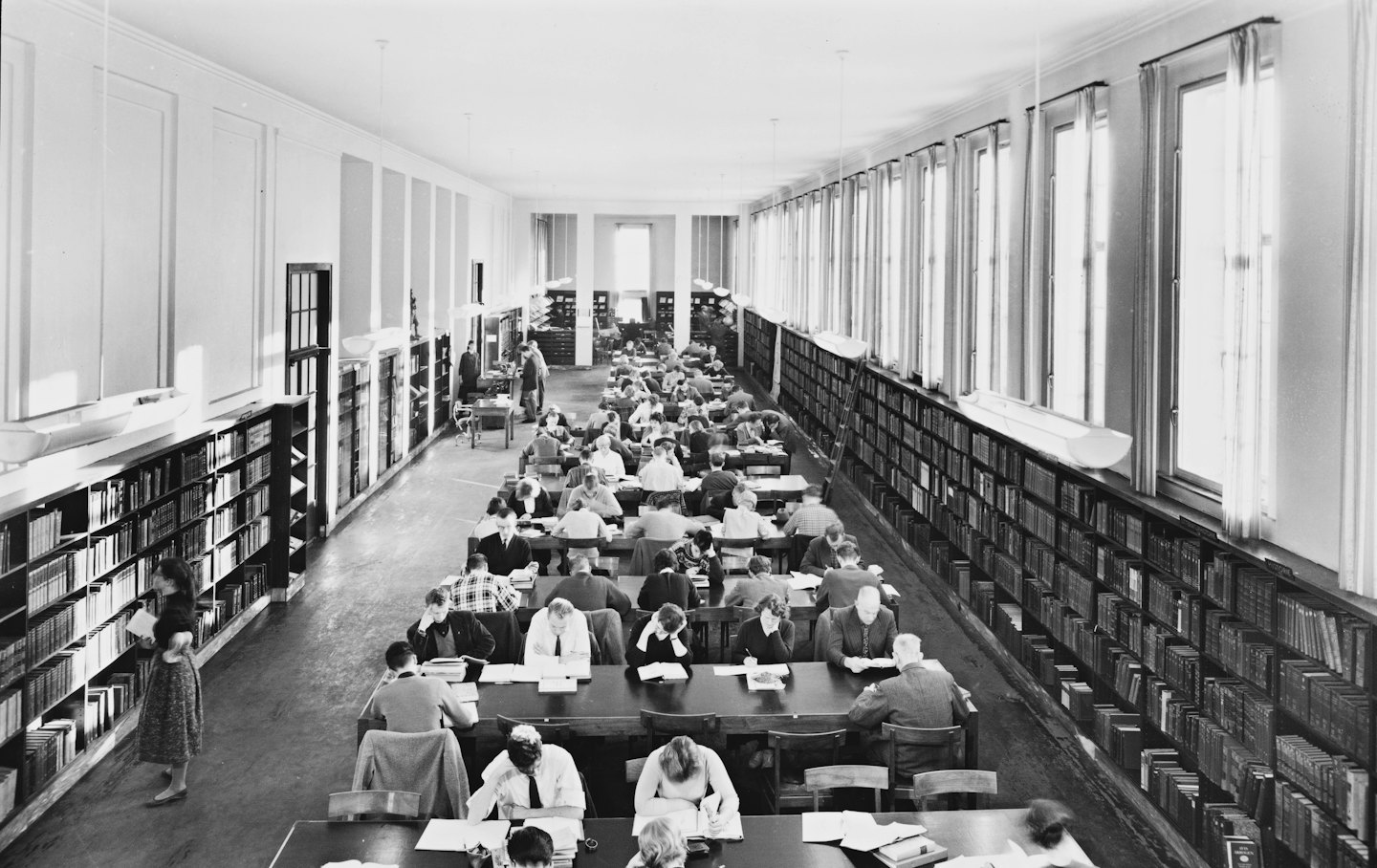 Dorośli uczą się i czytają książki w dużej czytelni bibliotecznej.